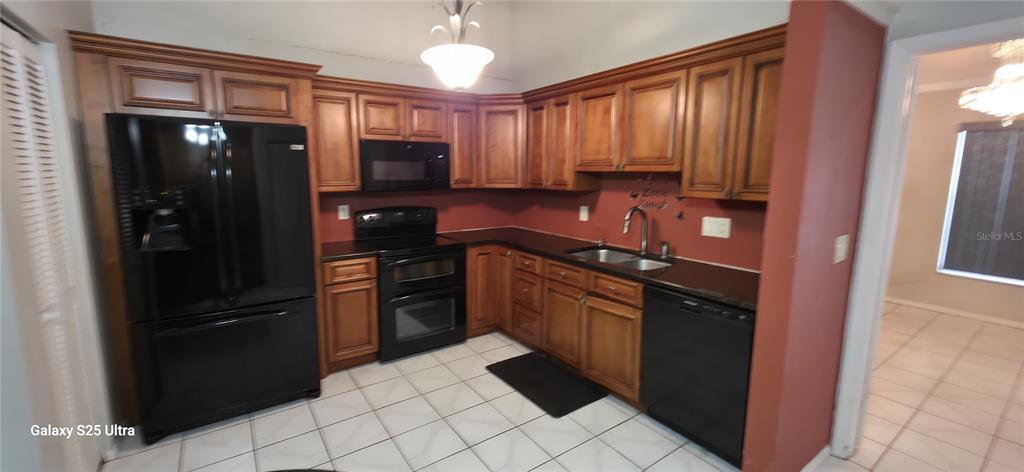 A kitchen features wood cabinets, black appliances, dark countertops, and white tile flooring — 3205 LAUREL DALE DRIVE, TAMPA, FL
