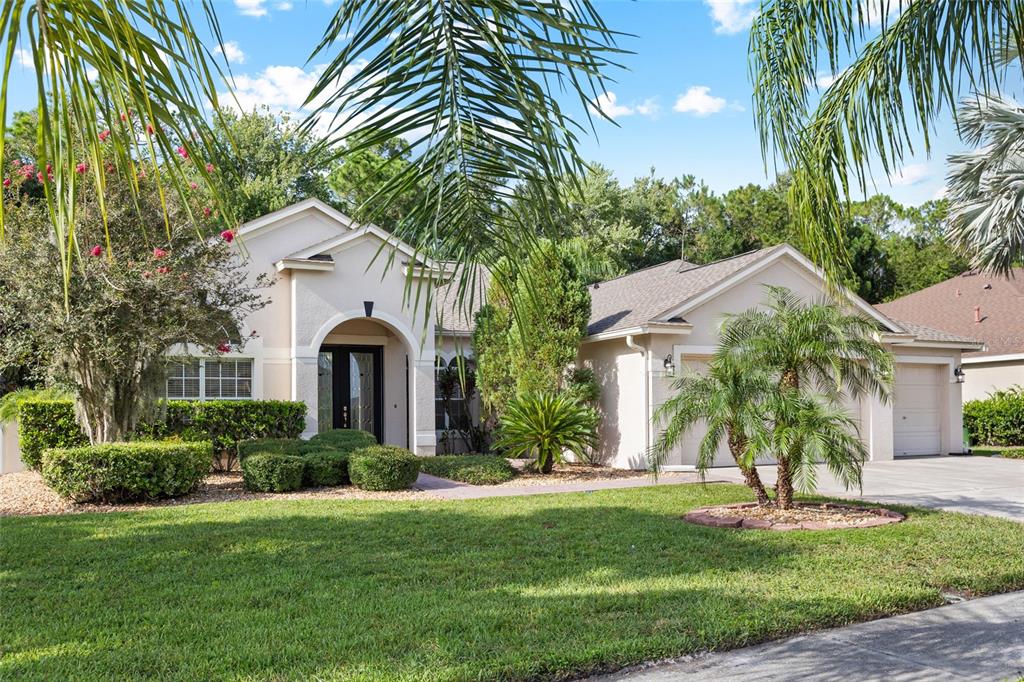 A single-story beige house with a front-facing garage, arched entryway, and landscaped front yard — 16132 IVY LAKE DRIVE, ODESSA, FL