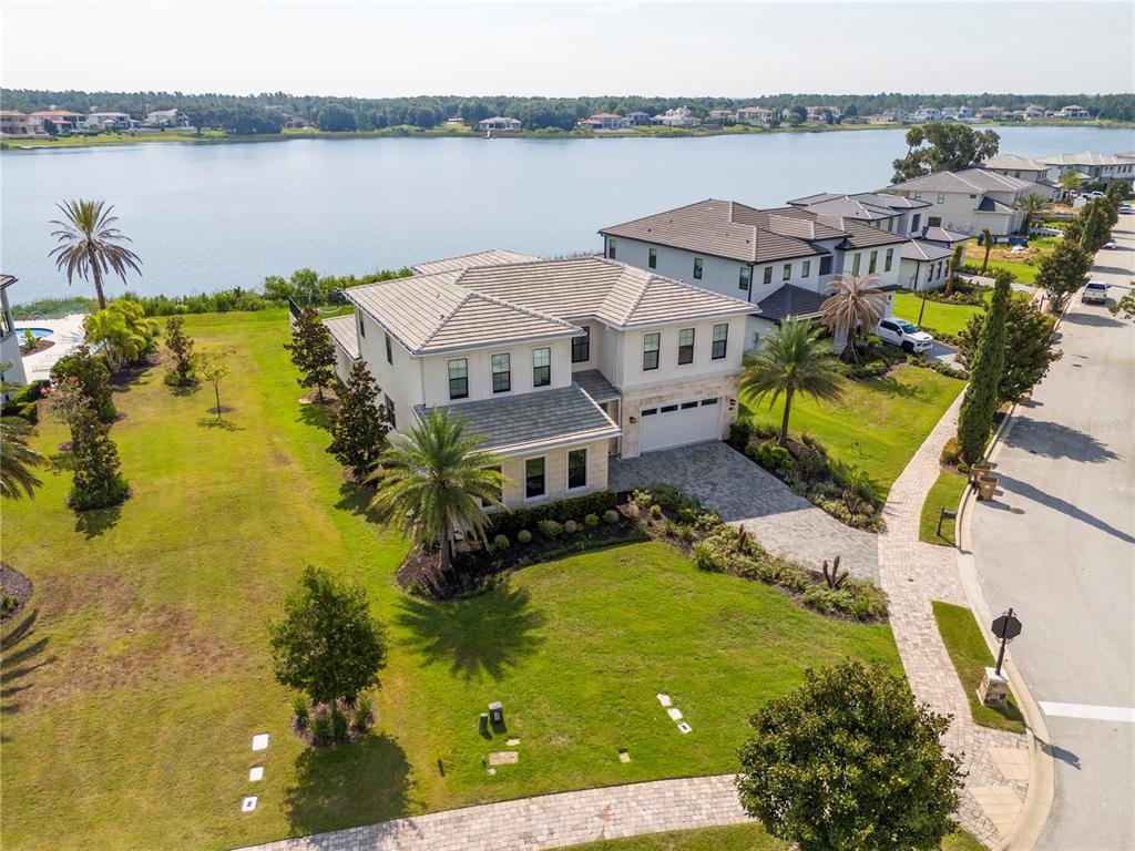 An aerial view shows a two-story house with a tile roof and a lakefront backyard — 16744 BOLSENA DRIVE, BELLA COLLINA, FL