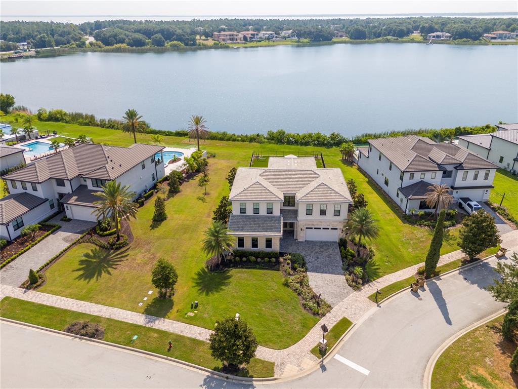 An aerial view shows a two-story house with a paved driveway facing a large lake — 16744 BOLSENA DRIVE, BELLA COLLINA, FL