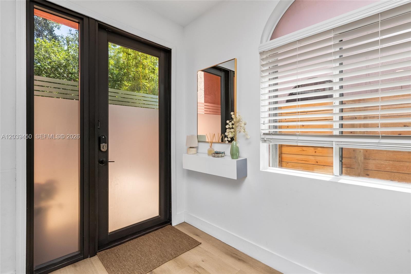 An entryway features a black-framed glass door, a floating shelf, a mirror, and a window — 3125 Jackson Ave # 3125, Miami FL 33133, MIAMI, FL