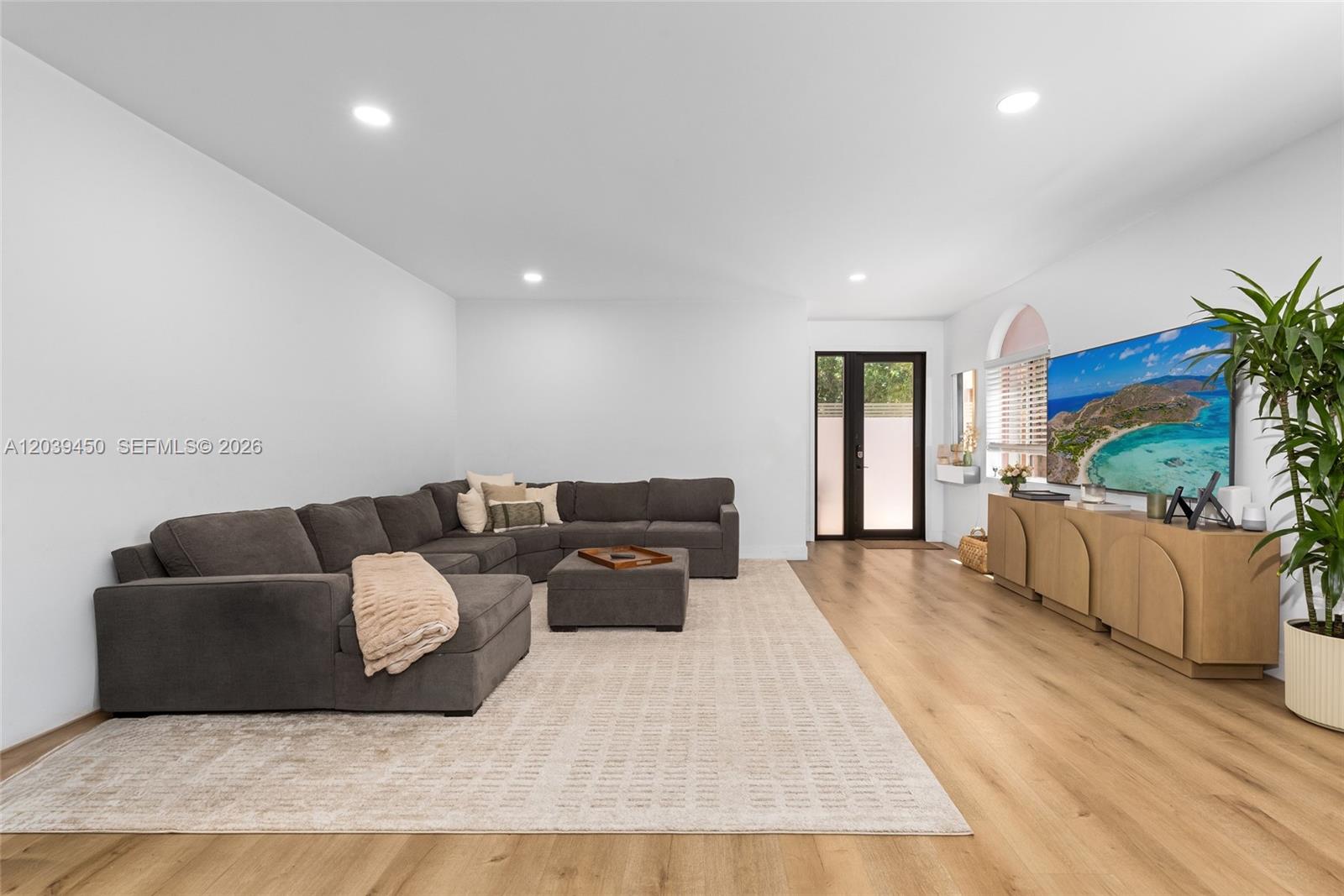 A living room features a large gray sectional sofa, a television, and light wood flooring — 3125 Jackson Ave # 3125, Miami FL 33133, MIAMI, FL