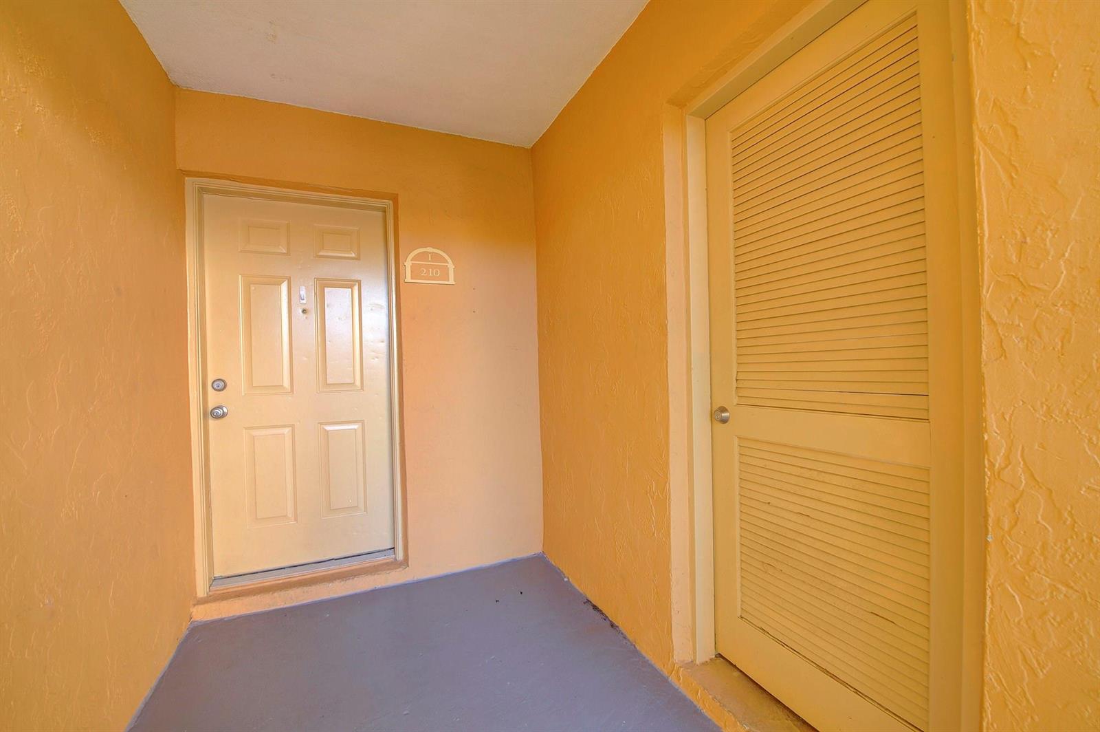 An exterior entryway features a light-colored door labeled 210, a louvered closet door, and walls — 18111 NW 68th Avenue # I210, Hialeah FL 33015, HIALEAH, FL