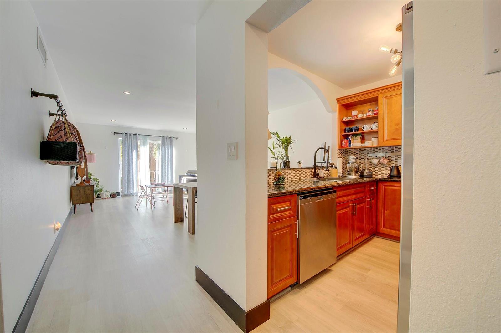 A view from a hallway into a kitchen with wood cabinets and an adjacent living area — 18111 NW 68th Avenue # I210, Hialeah FL 33015, HIALEAH, FL