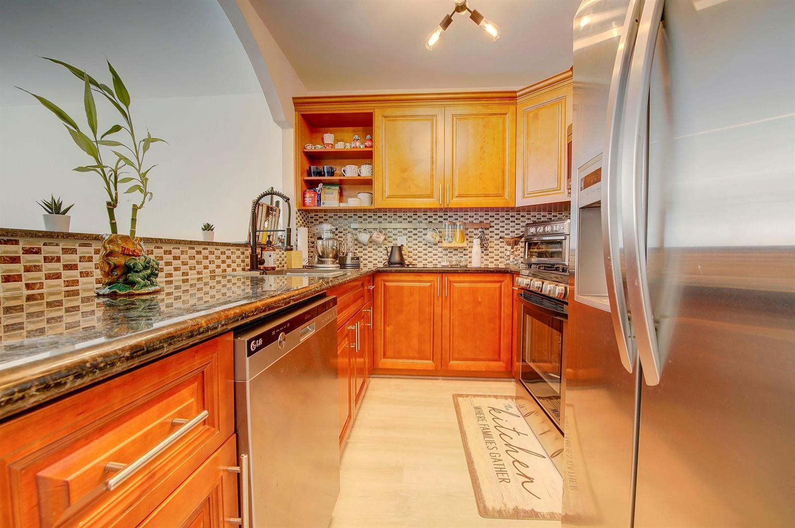 A kitchen features wood cabinets, granite countertops, stainless steel appliances, and a tiled backsplash — 18111 NW 68th Avenue # I210, Hialeah FL 33015, HIALEAH, FL