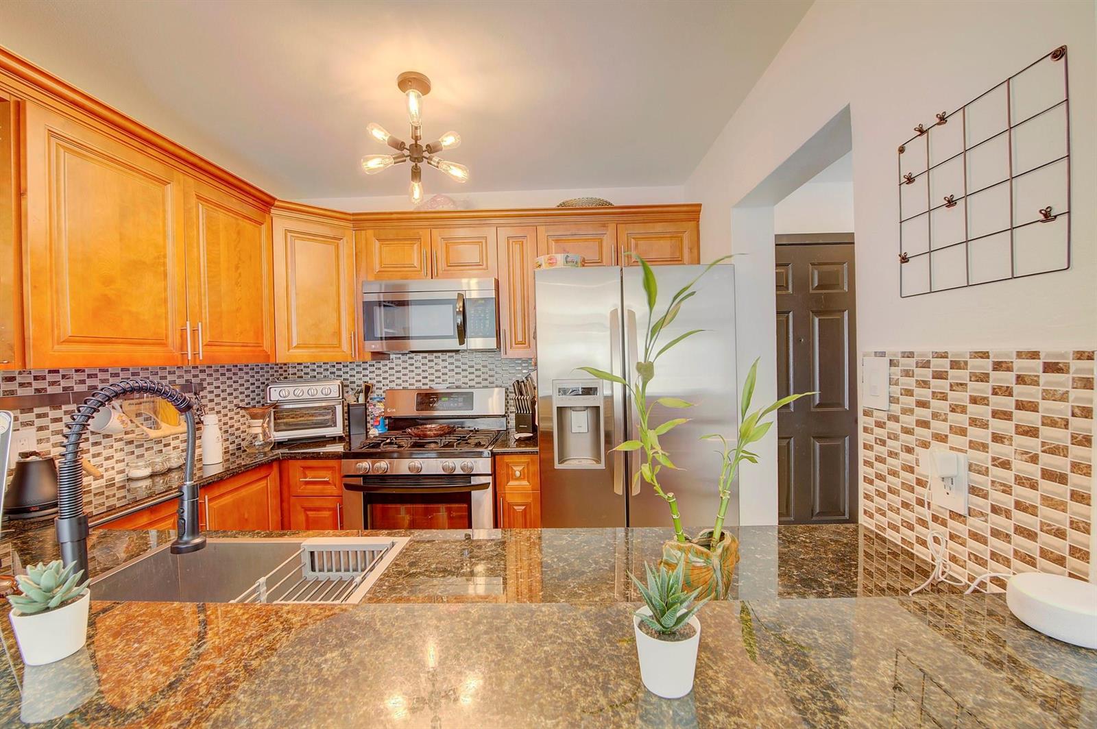 A kitchen features wood cabinets, stainless steel appliances, granite countertops, and a tile backsplash — 18111 NW 68th Avenue # I210, Hialeah FL 33015, HIALEAH, FL
