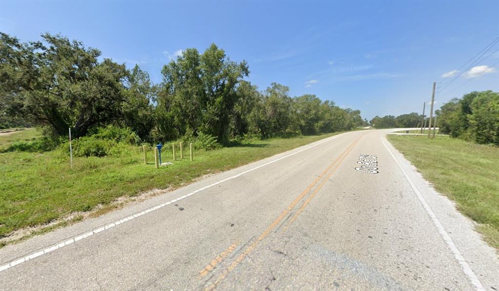 A paved road runs alongside a grassy area with trees and a blue utility post — SW CO ROAD 761, ARCADIA, FL