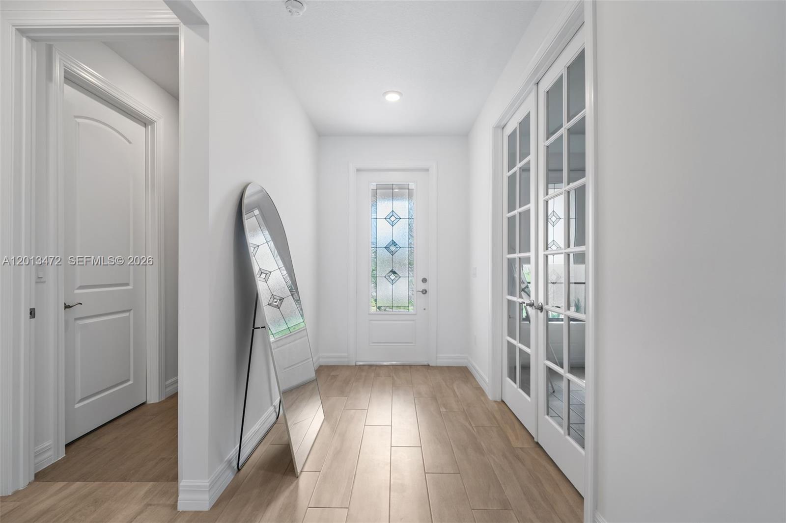 A bright entryway features light wood-look tile flooring, a floor mirror, and glass-paneled doors — 2715 Primrose Pl, Oakland Park FL 33309, OAKLAND PARK, FL