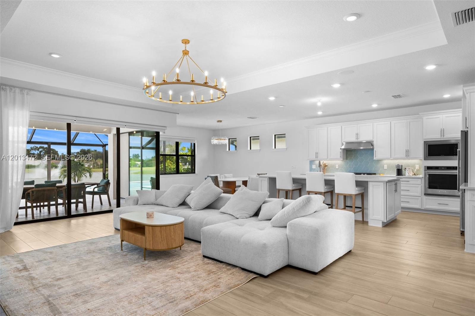 A bright open-concept living room and kitchen featuring white cabinetry, a large sectional, and chandelier — 2715 Primrose Pl, Oakland Park FL 33309, OAKLAND PARK, FL