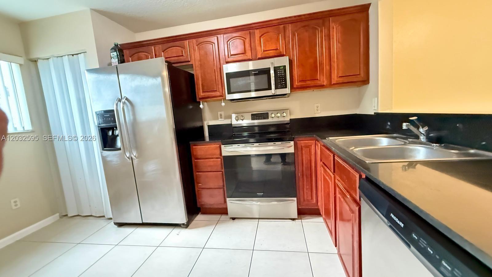 A kitchen features stainless steel appliances, dark countertops, and wood cabinets over tiled floors — 6631 Winfield Blvd # 6, Margate FL 33063, MARGATE, FL