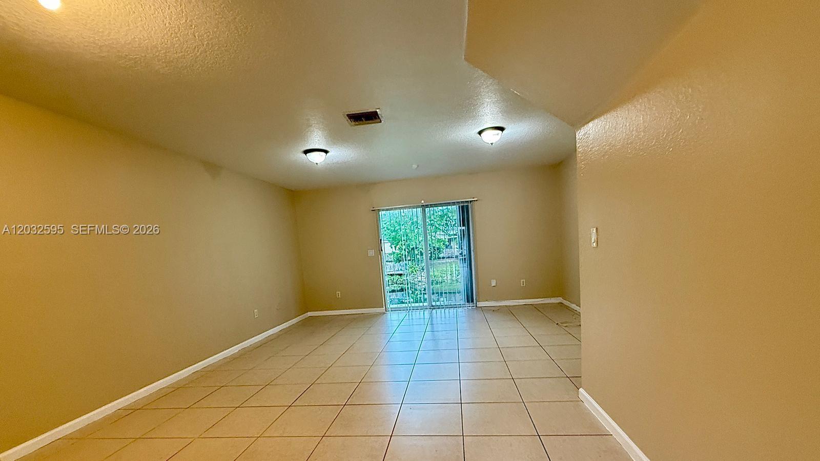 An empty living room features beige walls, tile flooring, and sliding glass doors to outside — 6631 Winfield Blvd # 6, Margate FL 33063, MARGATE, FL