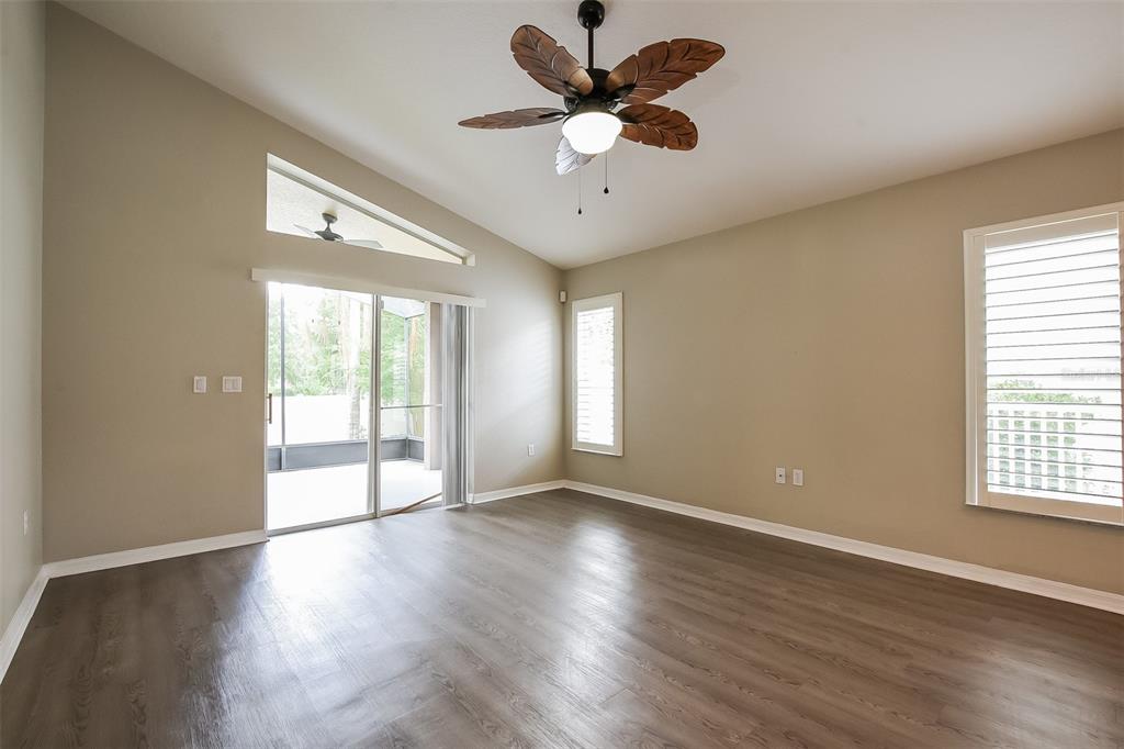 An empty living room features wood-look flooring, a vaulted ceiling, and a palm-leaf ceiling fan — 3136 LINDERA DRIVE, DELTONA, FL