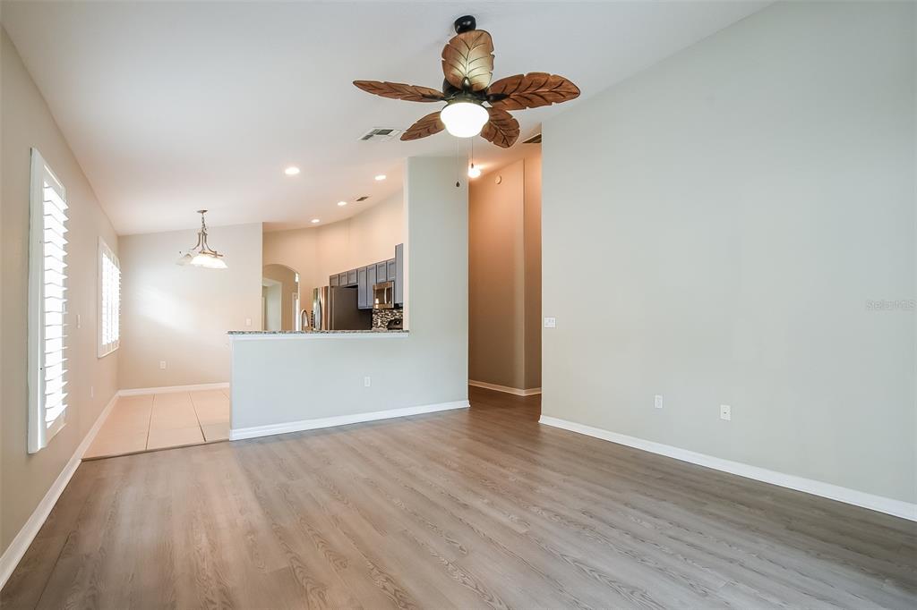 A living room with wood-look flooring, a ceiling fan, and an adjacent kitchen area — 3136 LINDERA DRIVE, DELTONA, FL