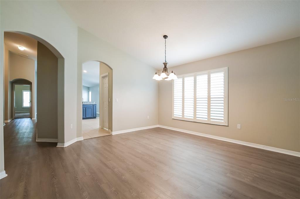 An empty dining room features light wood-look flooring, beige walls, and a multi-light chandelier — 3136 LINDERA DRIVE, DELTONA, FL