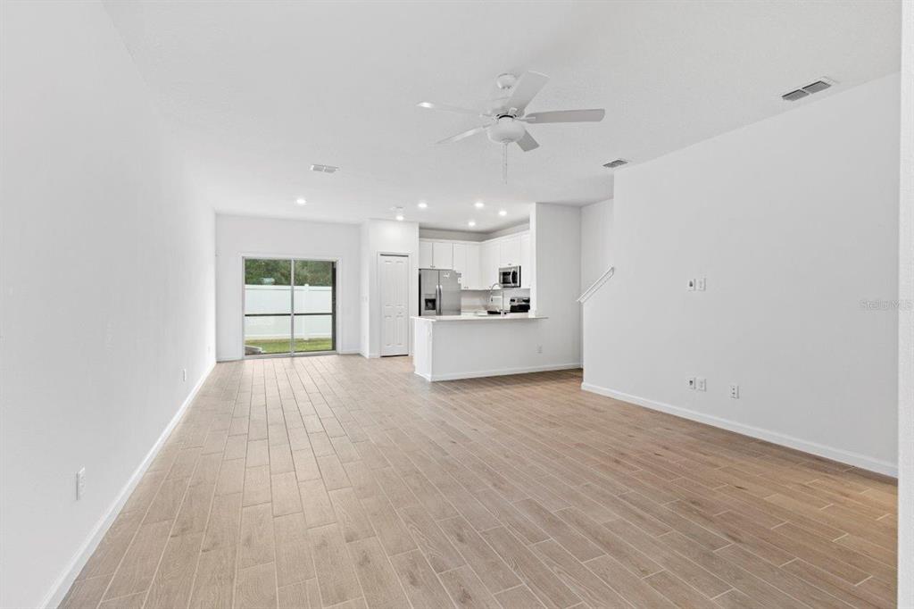 An open-concept living area features light wood-look tile flooring, a ceiling fan, and a kitchen — 698 NW 126TH TERRACE, NEWBERRY, FL