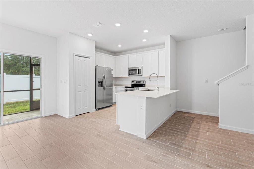 A modern kitchen features white cabinetry, stainless steel appliances, and light wood-look tile flooring — 698 NW 126TH TERRACE, NEWBERRY, FL