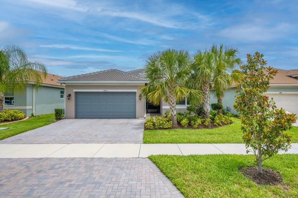 A single-story house with a gray garage, a paved driveway, and palm trees in the front — 4844 AVILA LAKES DRIVE, WIMAUMA, FL
