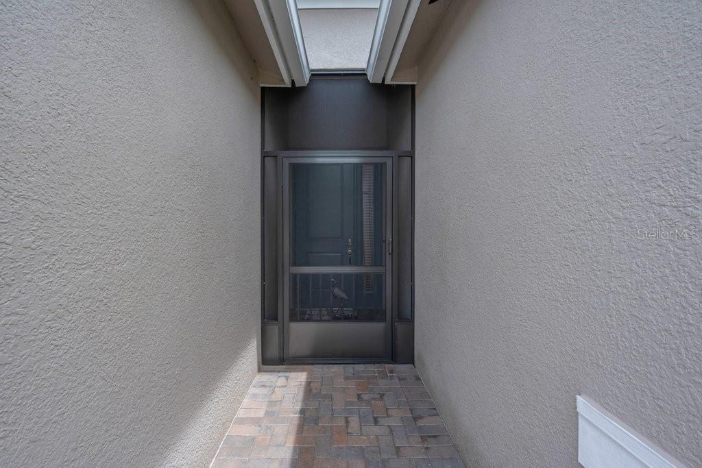 A narrow entryway features a paver floor, stucco walls, and a dark screen door — 4844 AVILA LAKES DRIVE, WIMAUMA, FL