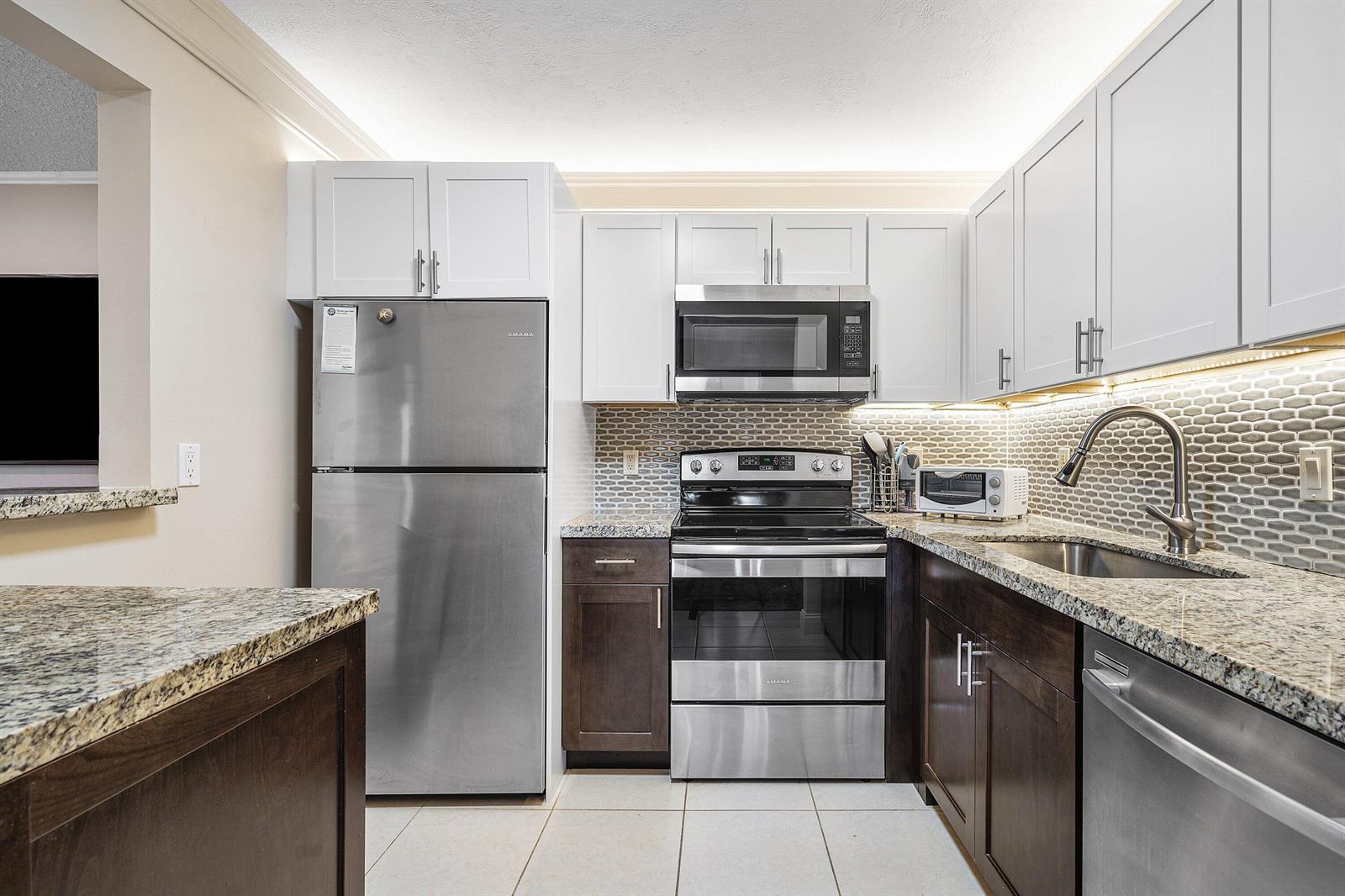 A kitchen features white upper cabinets, dark lower cabinets, granite countertops, and stainless steel appliances — 142 Brittany Terrace, Delray Beach FL 33446, DELRAY BEACH, FL