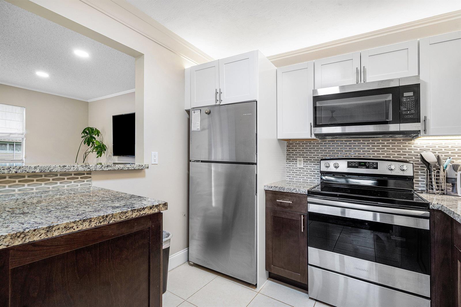 A kitchen features stainless steel appliances, white upper cabinets, dark lower cabinets, and granite countertops — 142 Brittany Terrace, Delray Beach FL 33446, DELRAY BEACH, FL