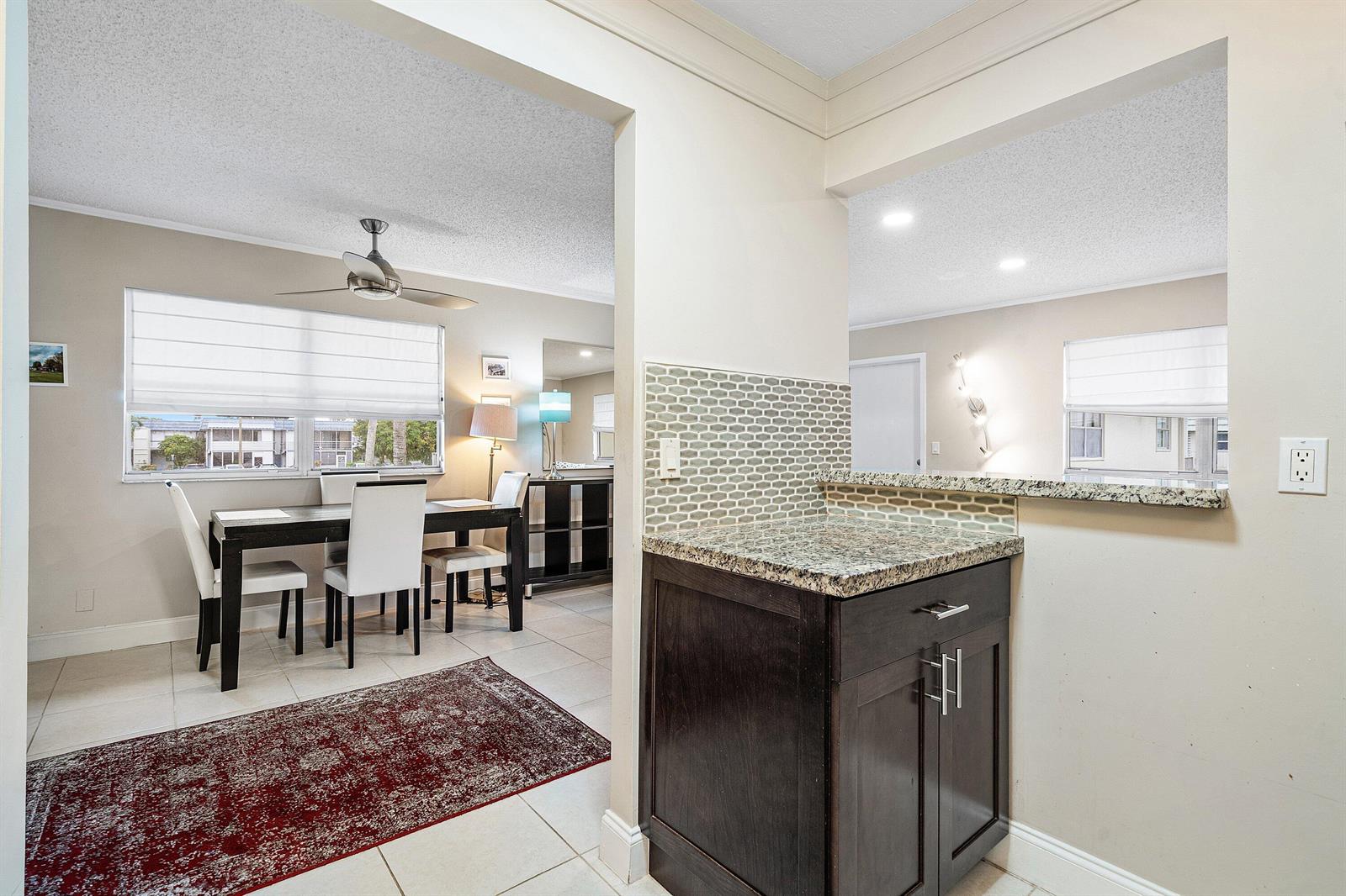 A dining area with a ceiling fan and a kitchen pass-through with dark cabinetry — 142 Brittany Terrace, Delray Beach FL 33446, DELRAY BEACH, FL