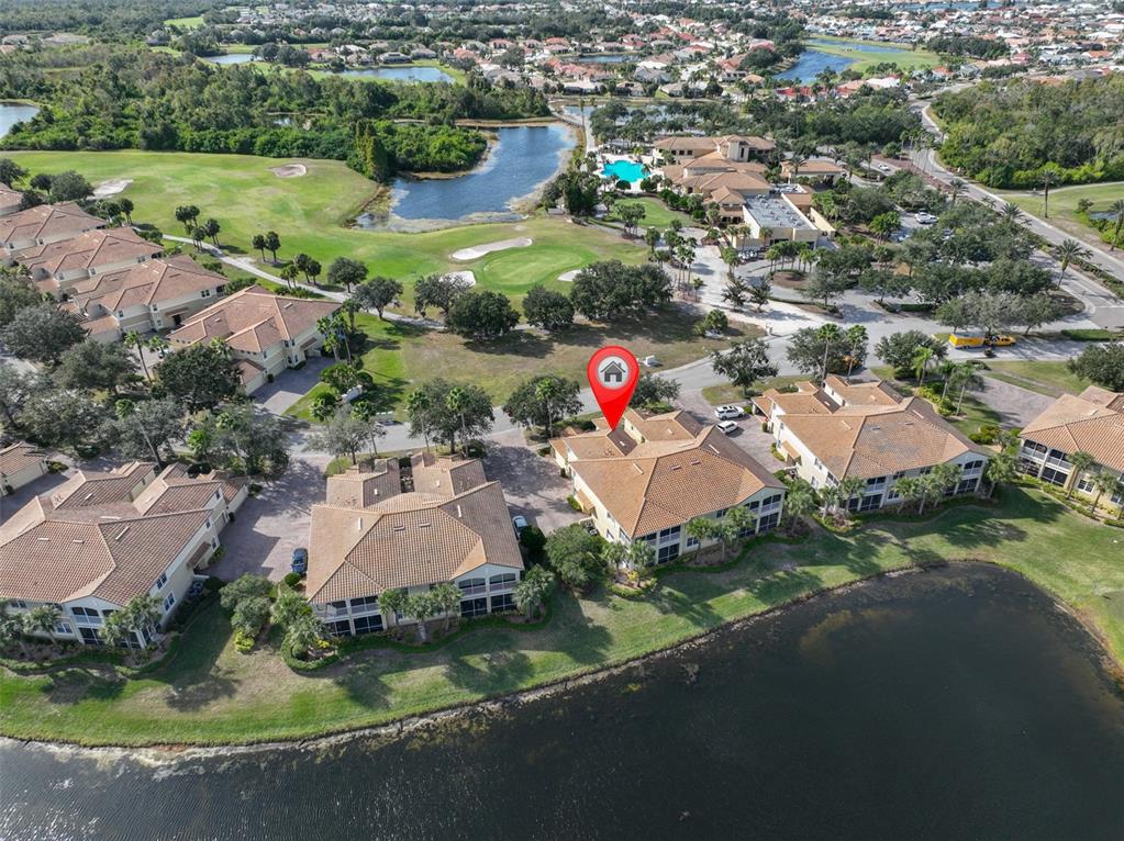 An aerial view shows multi-story residential buildings with tile roofs situated beside a lake — 1324 EMERALD DUNES DRIVE, SUN CITY CENTER, FL