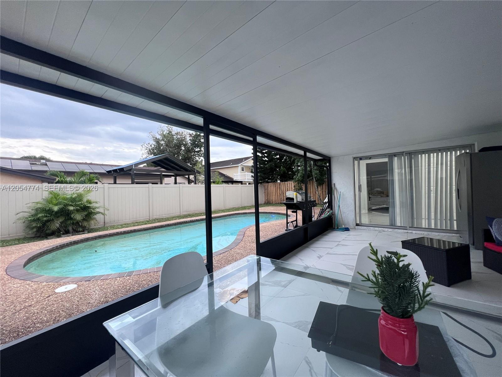 A covered patio features a glass dining table, white tile flooring, and a swimming pool — 2001 SW 85th Ave, North Lauderdale FL 33068, NORTH LAUDERDALE, FL