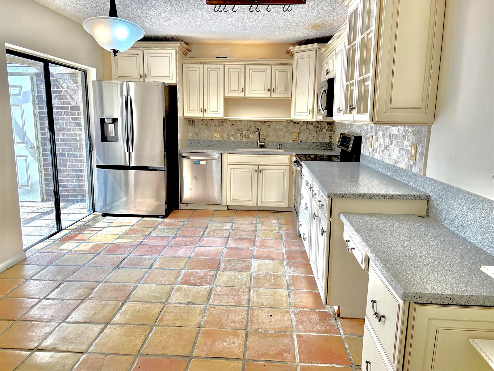 A kitchen features cream cabinets, stainless steel appliances, speckled countertops, and terracotta tile flooring — 511 5th Terrace, Palm Beach Gardens FL 33418, PALM BEACH GARDENS, FL