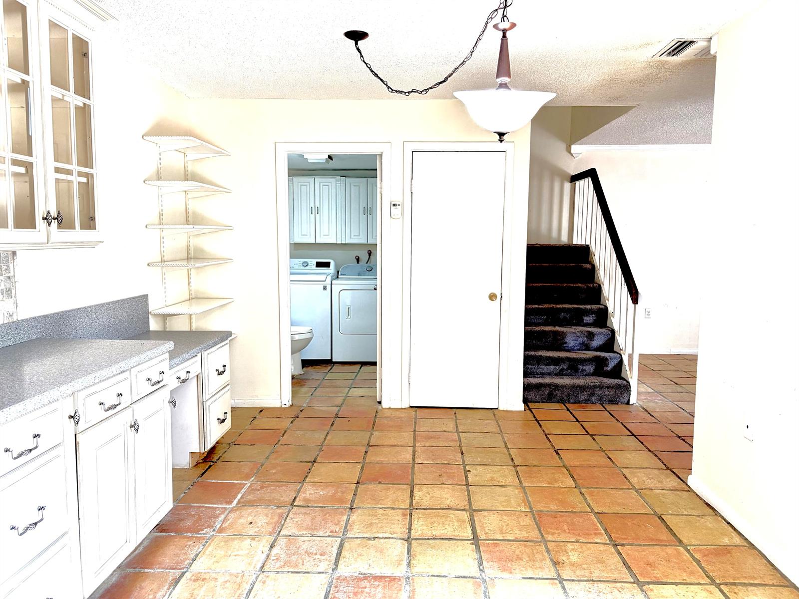A kitchen with white cabinets, terracotta tile flooring, and a doorway leading to a laundry room — 511 5th Terrace, Palm Beach Gardens FL 33418, PALM BEACH GARDENS, FL