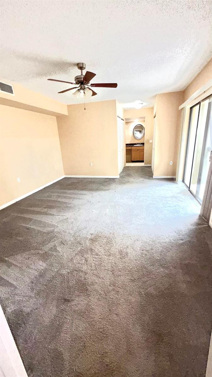 An empty room with beige walls, gray carpet, a ceiling fan, and a sliding door — 511 5th Terrace, Palm Beach Gardens FL 33418, PALM BEACH GARDENS, FL