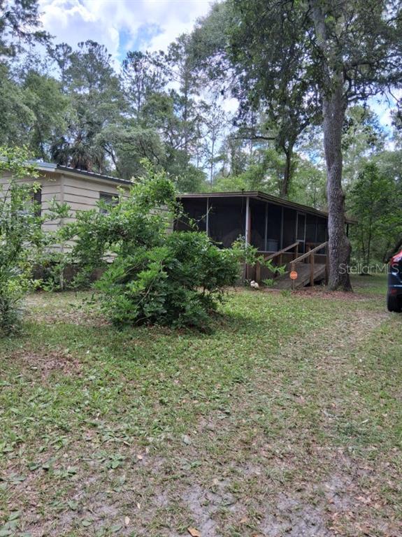A mobile home with a screened-in porch and a wooden ramp sits in a wooded yard — 13600 NE 166TH STREET, FORT MC COY, FL