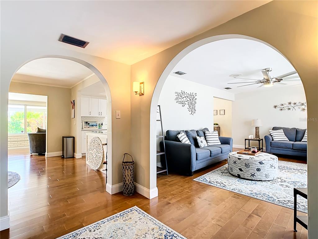 An interior view shows a living room and kitchen connected by arched doorways with hardwood floors — 2250 WATROUS DR, DUNEDIN, FL