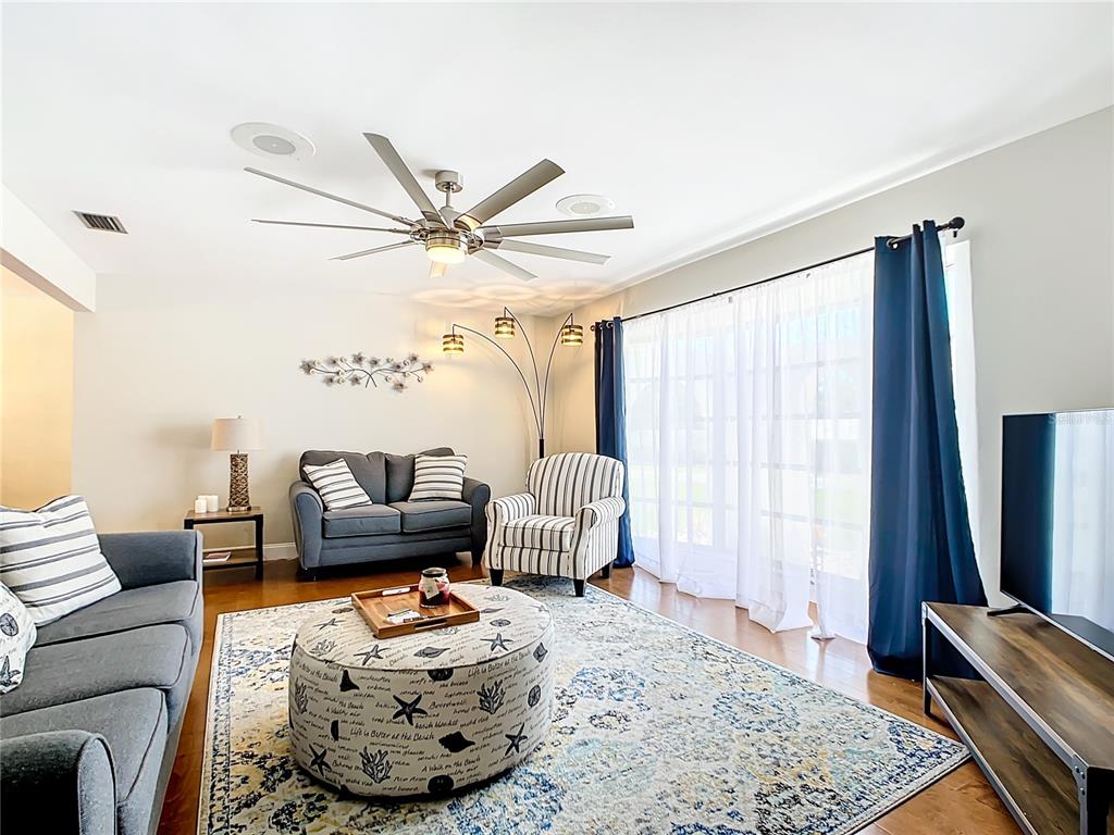 A living room features a gray sofa, striped armchair, patterned ottoman, and large sliding glass doors — 2250 WATROUS DR, DUNEDIN, FL