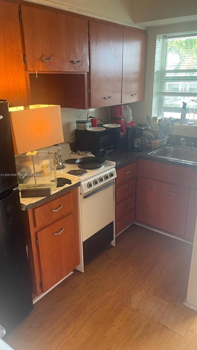 A kitchen features wood cabinets, a white stove, a black microwave, and a stainless sink — 2225 NE 123rd St # 204, North Miami FL 33181, NORTH MIAMI, FL