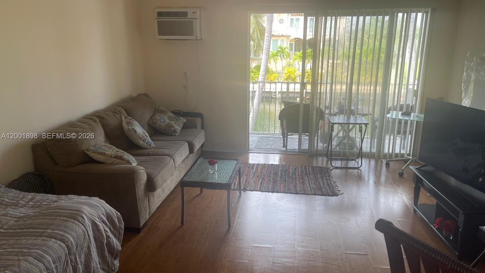 A living room features a brown sofa, glass coffee table, wood flooring, and a balcony view — 2225 NE 123rd St # 204, North Miami FL 33181, NORTH MIAMI, FL