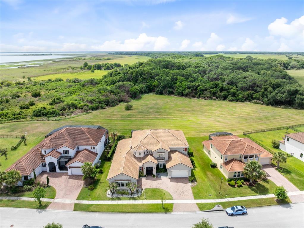 An aerial view shows three suburban houses situated in front of a large grassy field — 900 WINDLASS COURT, KISSIMMEE, FL