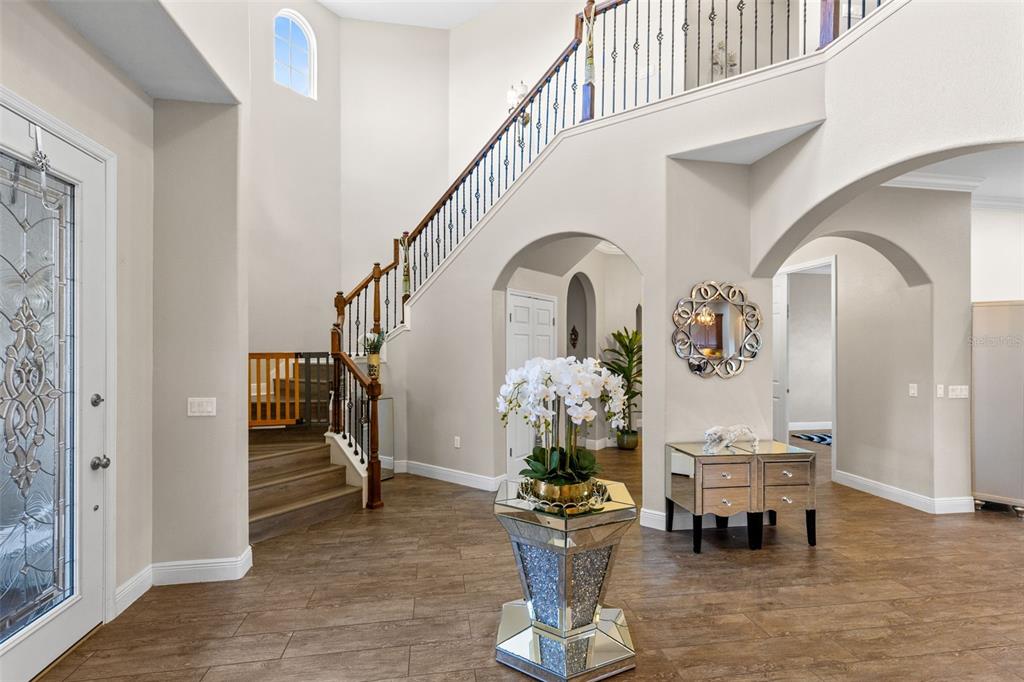A bright foyer features wood-look tile flooring, a grand staircase, and a mirrored pedestal table — 900 WINDLASS COURT, KISSIMMEE, FL