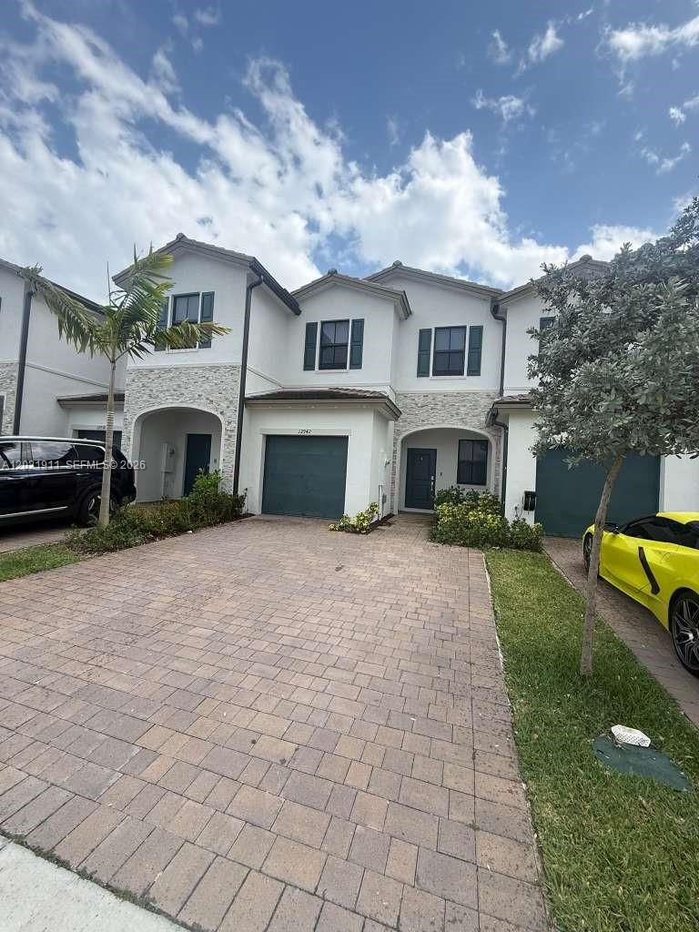 A two-story townhouse with a paved driveway, stone accents, and dark-colored garage doors — 12942 SW 231st St # 12942, Miami FL 33170, MIAMI, FL