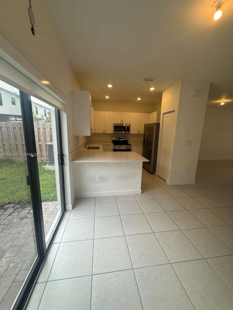 A kitchen with white cabinets, stainless steel appliances, and tile flooring overlooks a backyard — 12942 SW 231st St # 12942, Miami FL 33170, MIAMI, FL