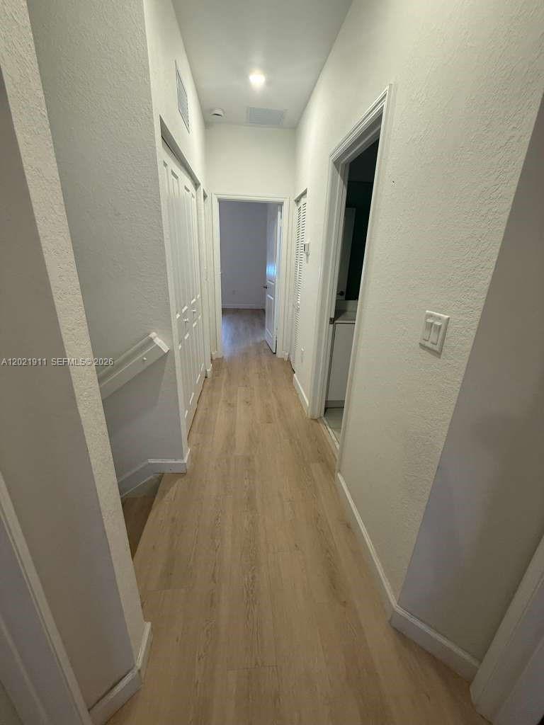 A narrow hallway features light wood-look flooring, white walls, and several closed doors — 12942 SW 231st St # 12942, Miami FL 33170, MIAMI, FL