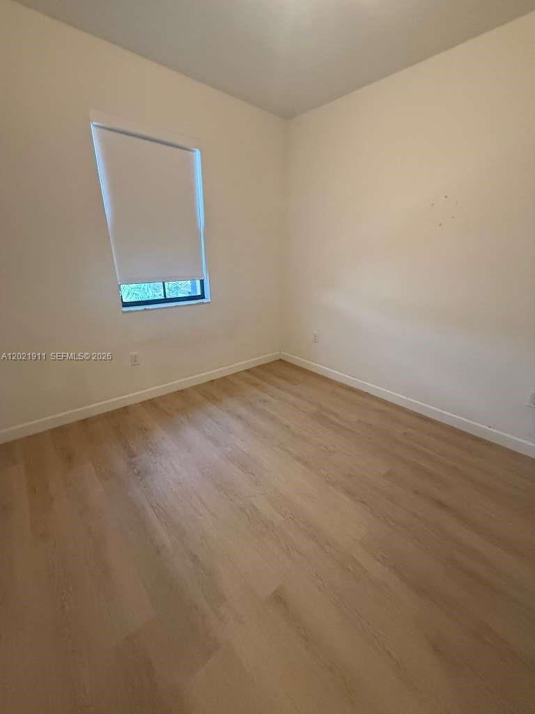 An empty bedroom features light-colored wood-look flooring, white walls, and a single window — 12942 SW 231st St # 12942, Miami FL 33170, MIAMI, FL