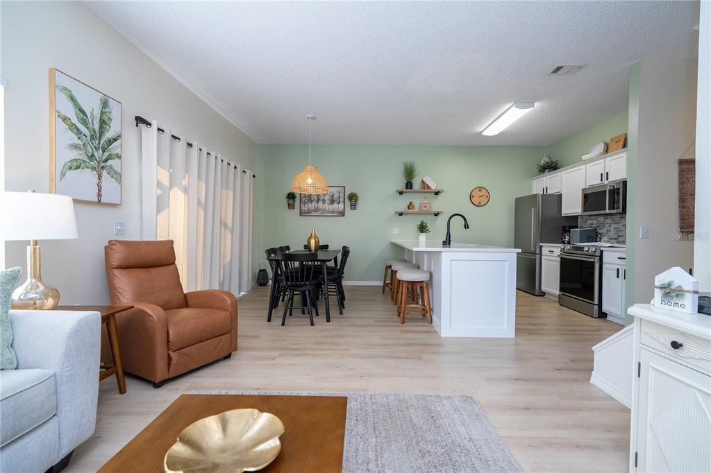 An open-concept kitchen and dining area features light wood flooring, white cabinetry, and green walls — 4722 FLAGLER BEACH WAY, KISSIMMEE, FL