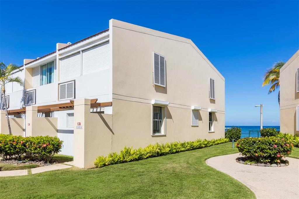 A beige two-story townhouse exterior features white trim, louvered shutters, and a landscaped lawn — Dorado del Mar Blvd OCEAN VILLAS UNIT 39, DORADO, PR