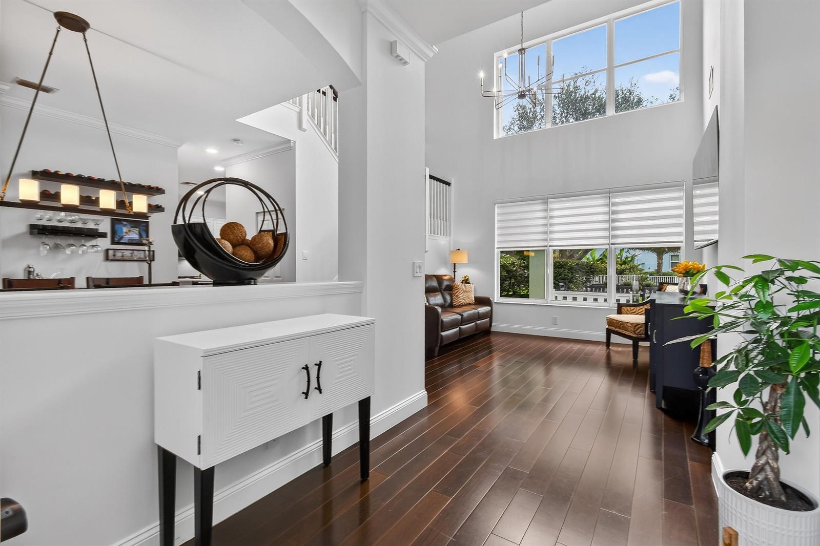 A bright living room features high ceilings, large windows, dark wood floors, and a white console — 265 Swallowtail Lane, Jupiter FL 33458, JUPITER, FL