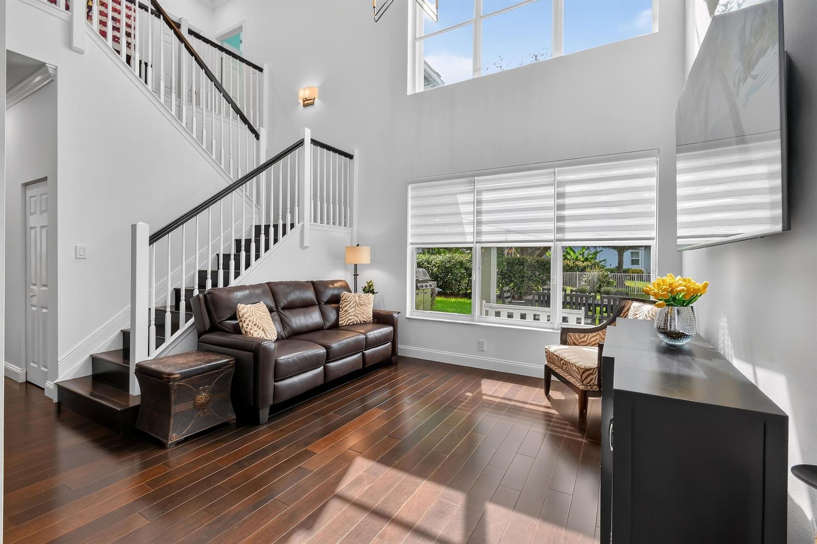 A living room with dark wood floors, a leather sofa, and a staircase with white railings — 265 Swallowtail Lane, Jupiter FL 33458, JUPITER, FL