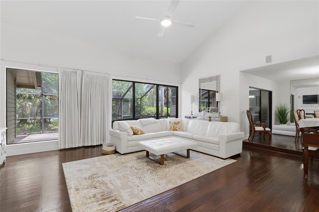 A living room with white walls, dark hardwood floors, a white sectional, and large windows — 5344 COBBLESTONE COURT, WESLEY CHAPEL, FL