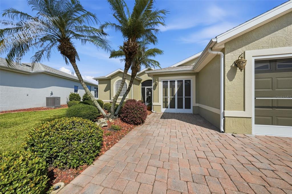 A paved walkway leads to a house entrance with palm trees and a garage door — 307 GRAND VISTA TRAIL, LEESBURG, FL