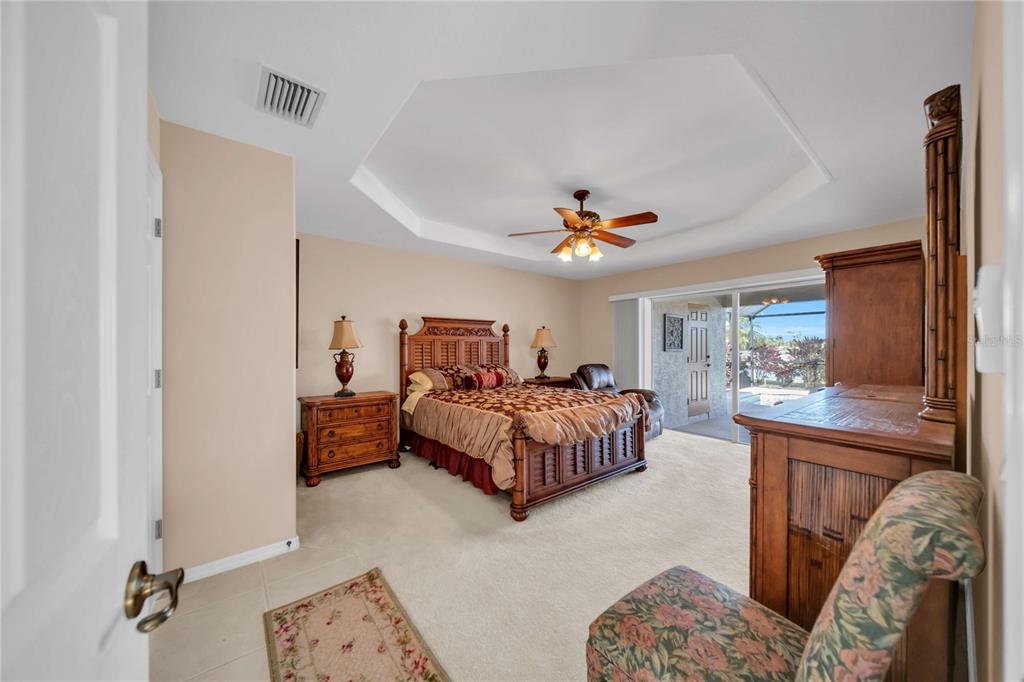 A bedroom with a tray ceiling, a wooden bed frame, and sliding glass doors — 240 WHITE MARSH LANE, ROTONDA WEST, FL
