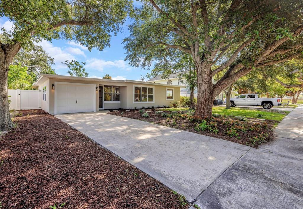 A single-story house with a white garage, concrete driveway, and large trees in the yard — 8017 31ST AVENUE N, ST PETERSBURG, FL
