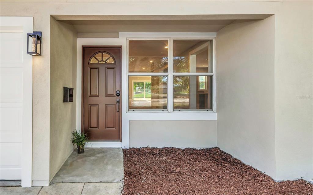 A brown front door sits next to a large window on a beige exterior wall — 8017 31ST AVENUE N, ST PETERSBURG, FL